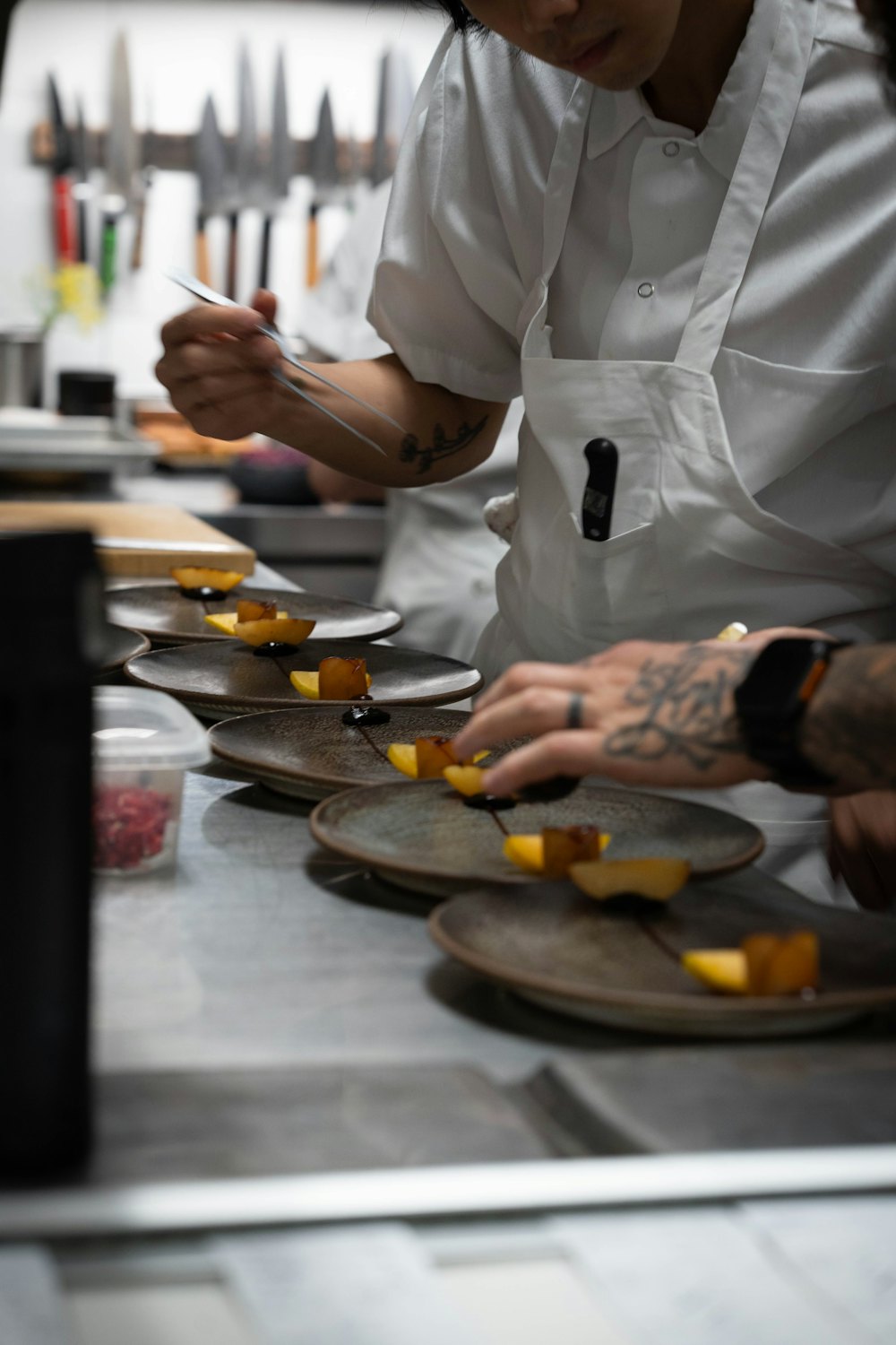 A chef plating a long row of identical dishes on a stainless-steel pass, banquet-style
